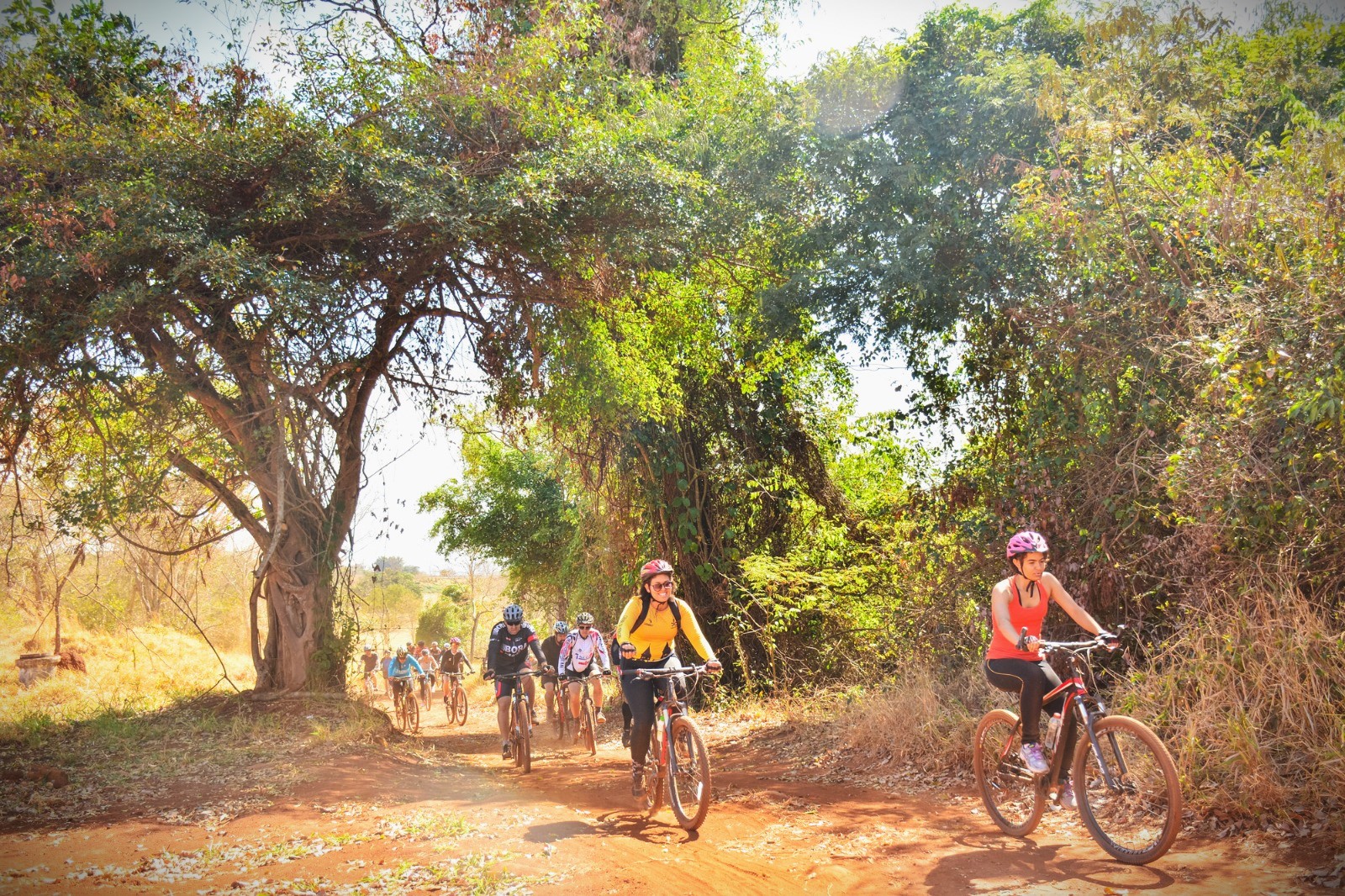 Imagem de vários ciclistas pedalando dentre as árvores e o chão de terra do Parque Bike, no Granja Marileusa